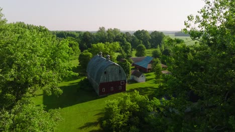 push in aerial drone shot between trees showing a barn on a farm