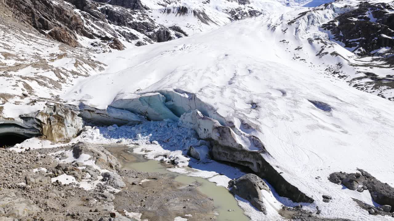 Morteratsch Glacier, icy tongue, crevasses, meltwater lake, and moraine, Bernina Range, Swiss Alps, Switzerland. Aerial drone backward