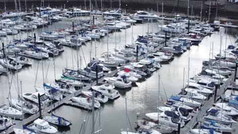 Scenic-luxurious-waterfront-harbour-apartment-village-yachts-and-sailboats-under-mountain-coastline-fly-over-tilt-down-aerial-view