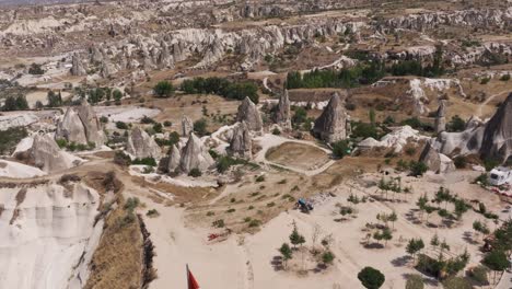 aerial pullback above valley overlook to turkish flag in cappadocia turkey with homes carved out of stone