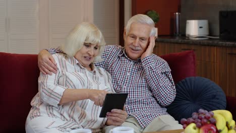 Pareja-De-Jubilados-Mayores-Con-Tableta-Digital-En-Casa.-Descansando-En-El-Sofá-En-La-Acogedora-Sala-De-Estar