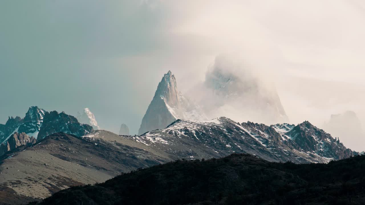 Epic, moody shot of the iconic Mount Fitz Roy and granite peaks partially covered by low-hanging clouds and mist. Captures the severe and atmospheric beauty of the high Patagonian Andes