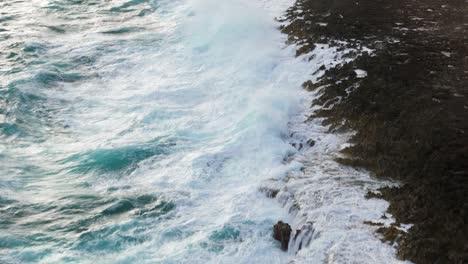 Waves-crash-churning-white-wash-across-heavily-eroded-limestone-rock-as-ocean-spray-rises-in-air