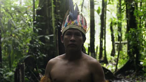 an indigenous guy wearing a feathered hat and fringed shirt in the dense forest in leticia, amazon, colombia