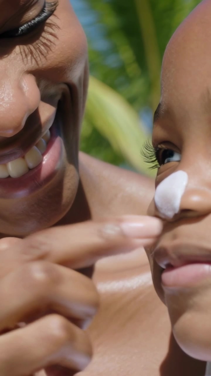 Vertical video: Noticing sun in yard, mother rubbing cream with fingertip on girl's nose, white top