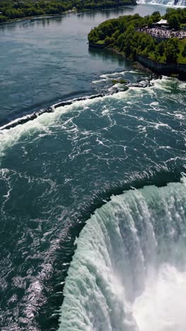 Aerial view of a powerful waterfall flowing into a river, surrounded by lush greenery