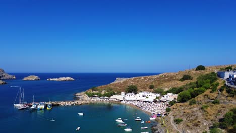 lindos beach and village in rhodes, greece with acropolis of lindos, houses and mediterranean sea during the day filmed with the drone