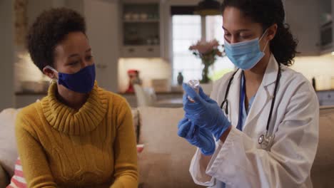 mixed race female doctor wearing face mask filling syringe at home