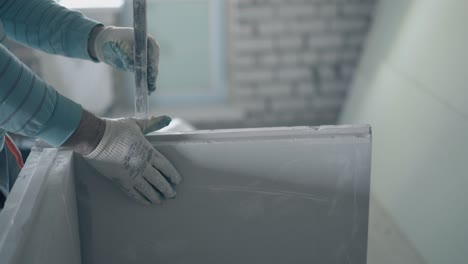 skilled painter in gloves measures white gypsum plasterboard