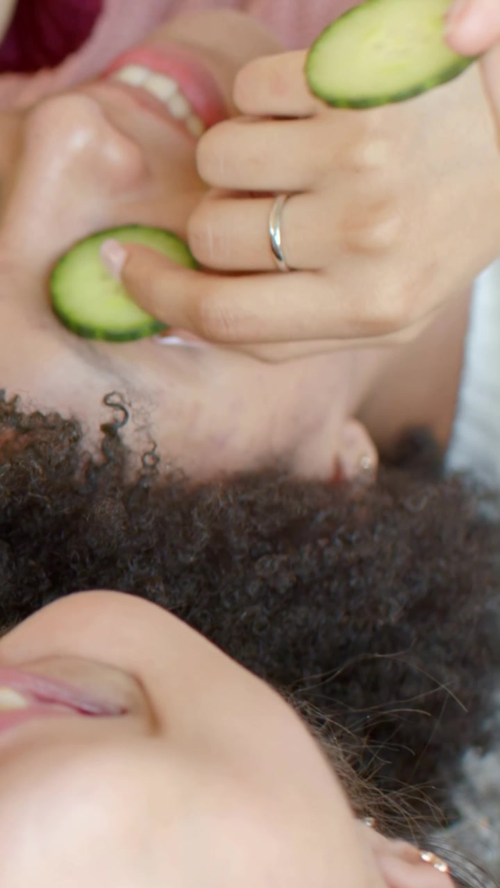 Video verticale: Mano inanellata che posiziona fette di cetriolo su una donna con i capelli ricci sul letto per la cura.