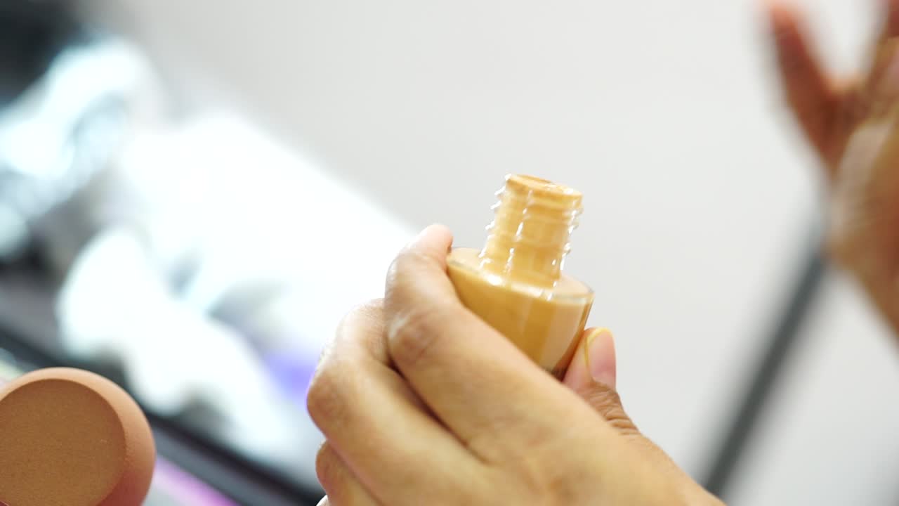 Female hands use bottle of beige liquid foundation make-up, close-up