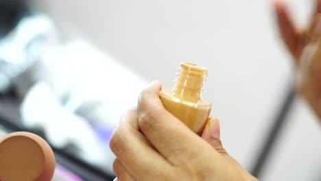 female hands use bottle of beige liquid foundation make-up, close-up