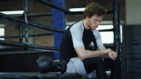 Sad-fighter-sitting-in-fitness-center.-Kickboxer-waiting-for-fight-at-gym