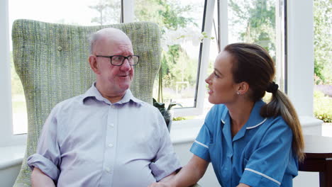 senior man sitting in chair and talking with nurse in retirement home