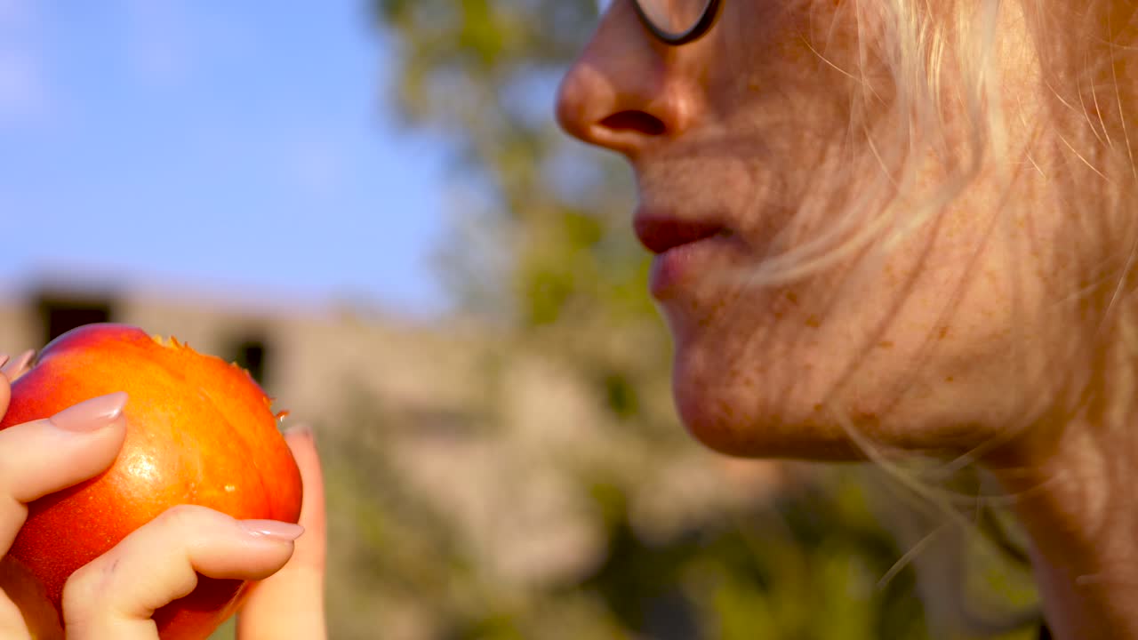 close up shot of young woman taking a bite of a peach