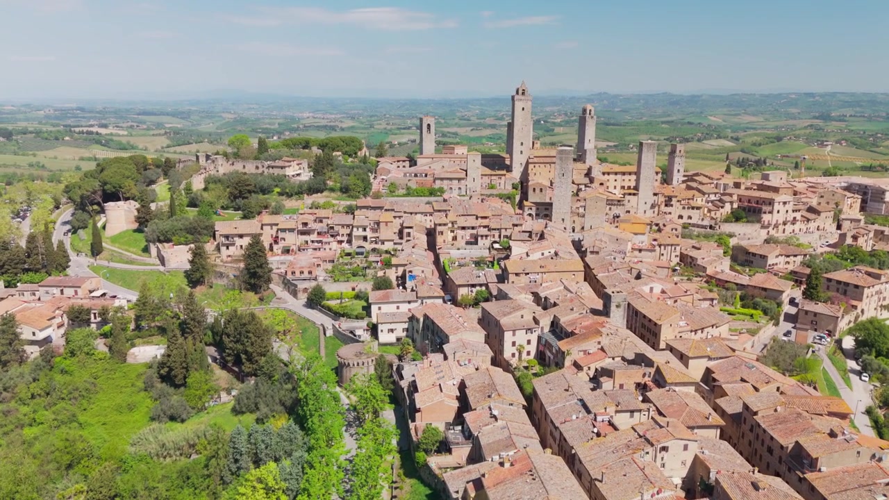 Drone che si muove a semicerchio sul centro di San Gimignano, Toscana, Italia, rivelando torri medievali, tetti caldi e la disposizione della città collinare nella morbida luce toscana.