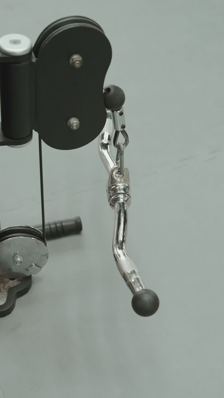 Close up of metal handle attachment connected to cable machine used for strength training in gym vertical