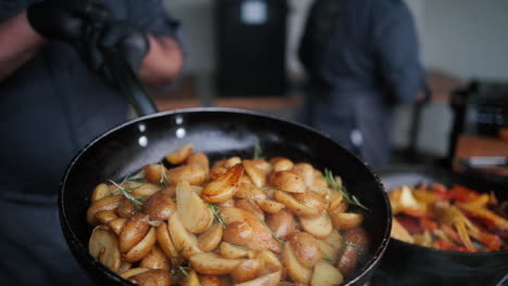 Chef-whipping-smoking-frying-Pan-with-rosemary-potatoes-on-gas-stove-at-outdoor-event