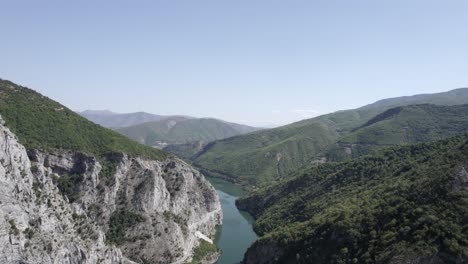 Drone-video-of-Plane-Discovery-ascending-over-the-Drin-River-at-the-Valbona-Pass-in-Kukes-County,-ending-up-showing-the-Ferry-stop-at-Komani-with-a-boat-sailing