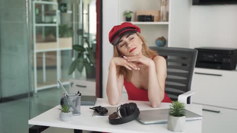 the young woman, a blonde in a red dress with red lips, sits dreamily at the table, resting her hands on her palms