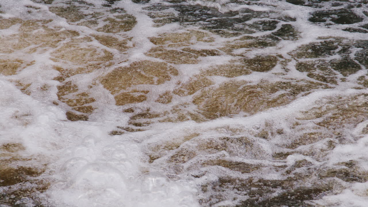 Swirling river surface filled with dense foam patterns and vivid bubbles in slowed motion conveying kinetic energy and texture