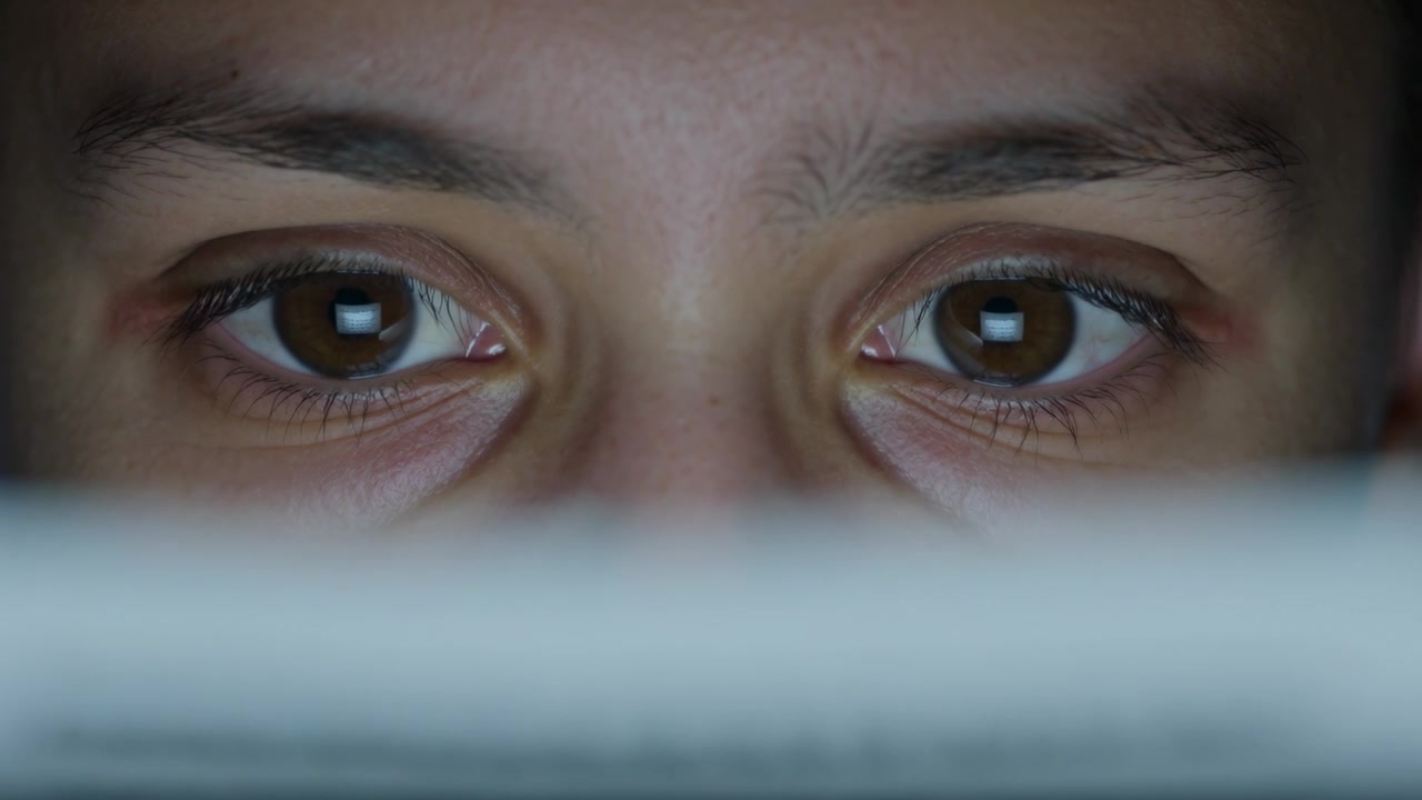Staring man reacting to bright screen in dim room, blinking and glancing down returning gaze, bezel