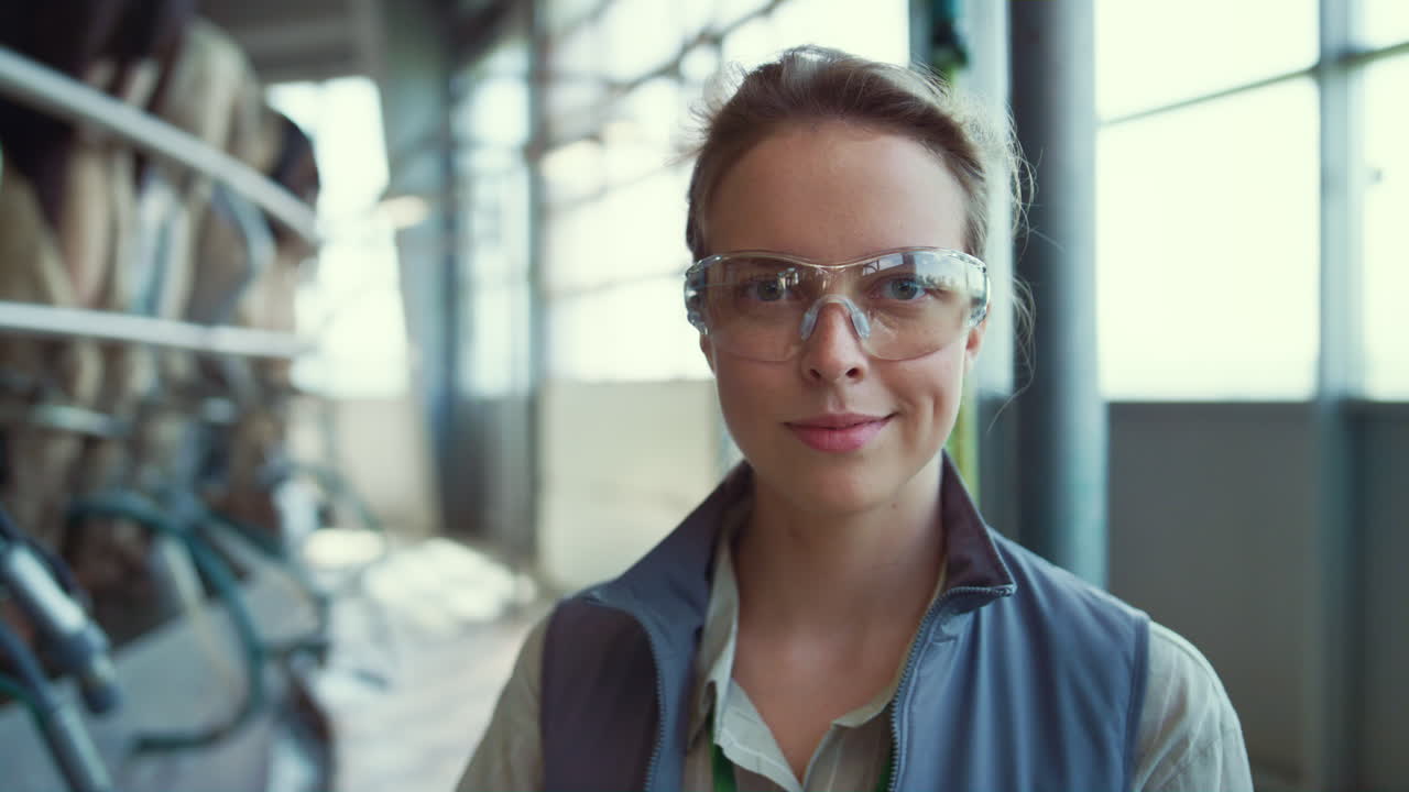 Closeup dairy farm worker in protective glasses posing at milking parlour alone.