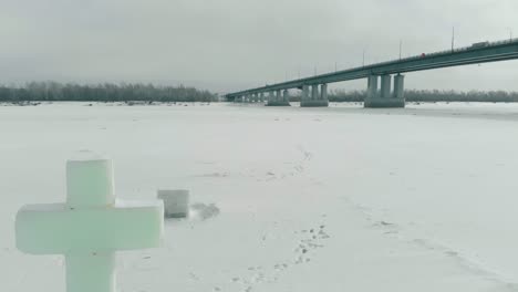carved ice cross on white frozen river with huge gray bridge