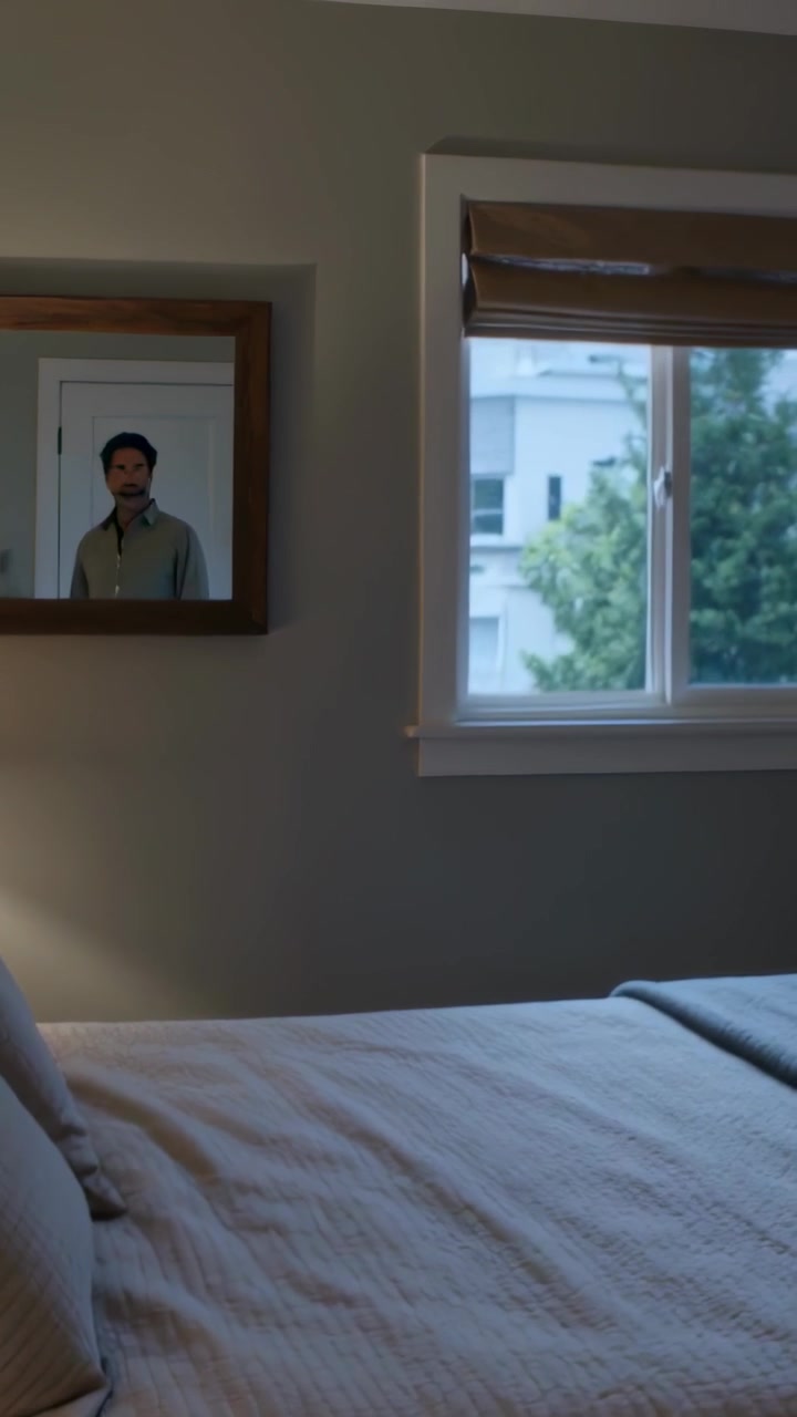 Vertical video: Pulling camera, man in shirt lifting hand off book at bedside mirror, copy space