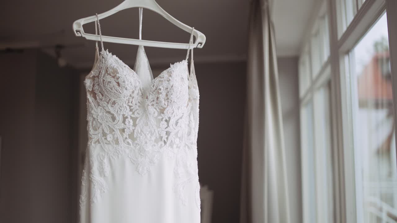 Close Up on elegant wedding dress on hanger next to window on wedding morning