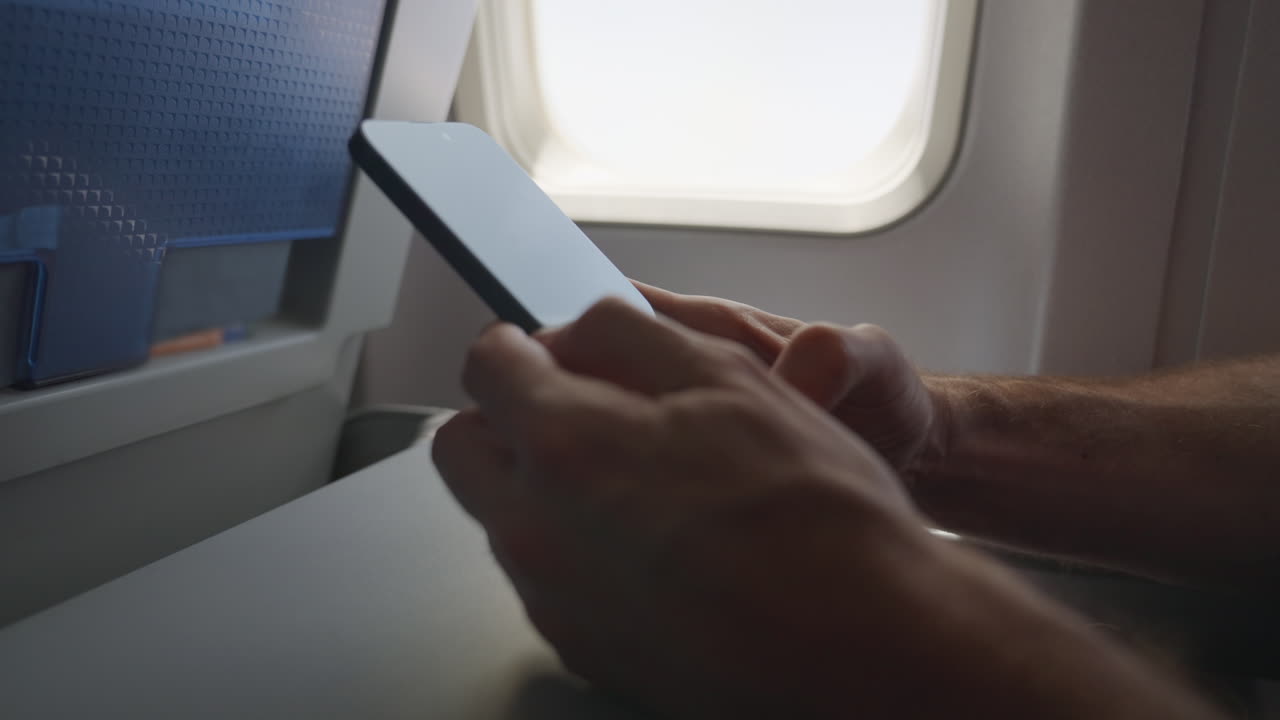 hombre usando un teléfono inteligente o móvil escribiendo y haciendo clic con la bandeja del asiento abierta y desplegada mientras está sentado en un vuelo comercial en un avión