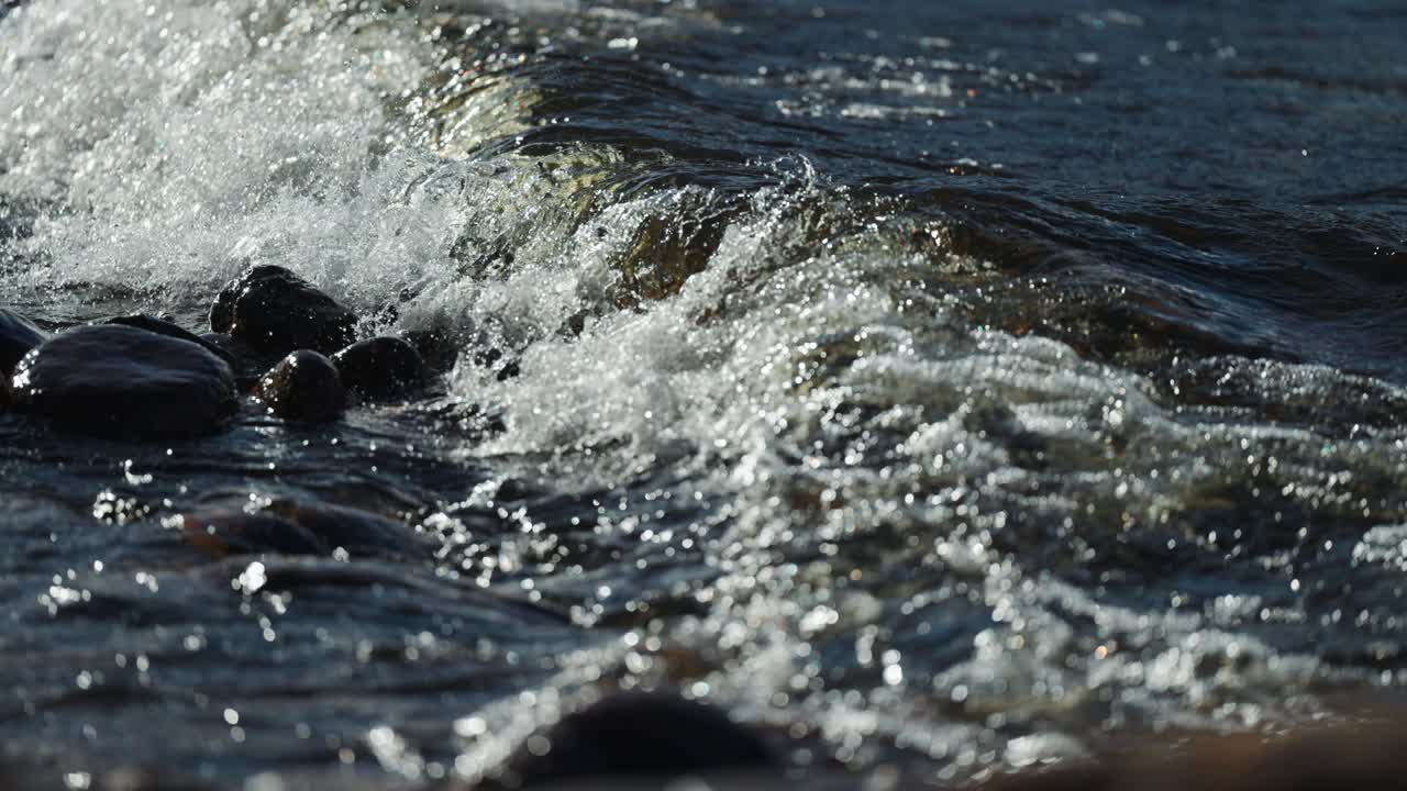 Waves roll and crush onto the pebble beach and rise water spray into the air