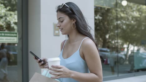 Young-woman-walking-along-street-and-typing-on-smartphone