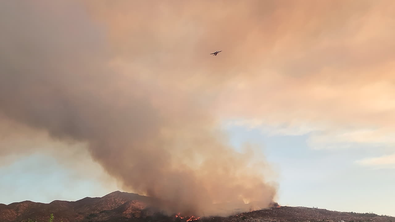 un avión de extinción de incendios vuela lejos de la columna de humo en los incendios forestales masivos cerca de hemet en el condado ribereño de california