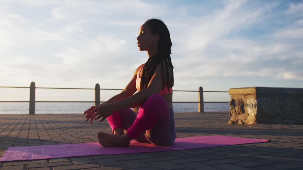 mujer afroamericana en ropa deportiva meditando en el paseo marítimo