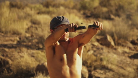 close up front view of a young shirtless american boy in sunglasses firing two handguns rapidly