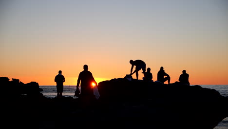 people watching sunset from rocks on beach silhouette