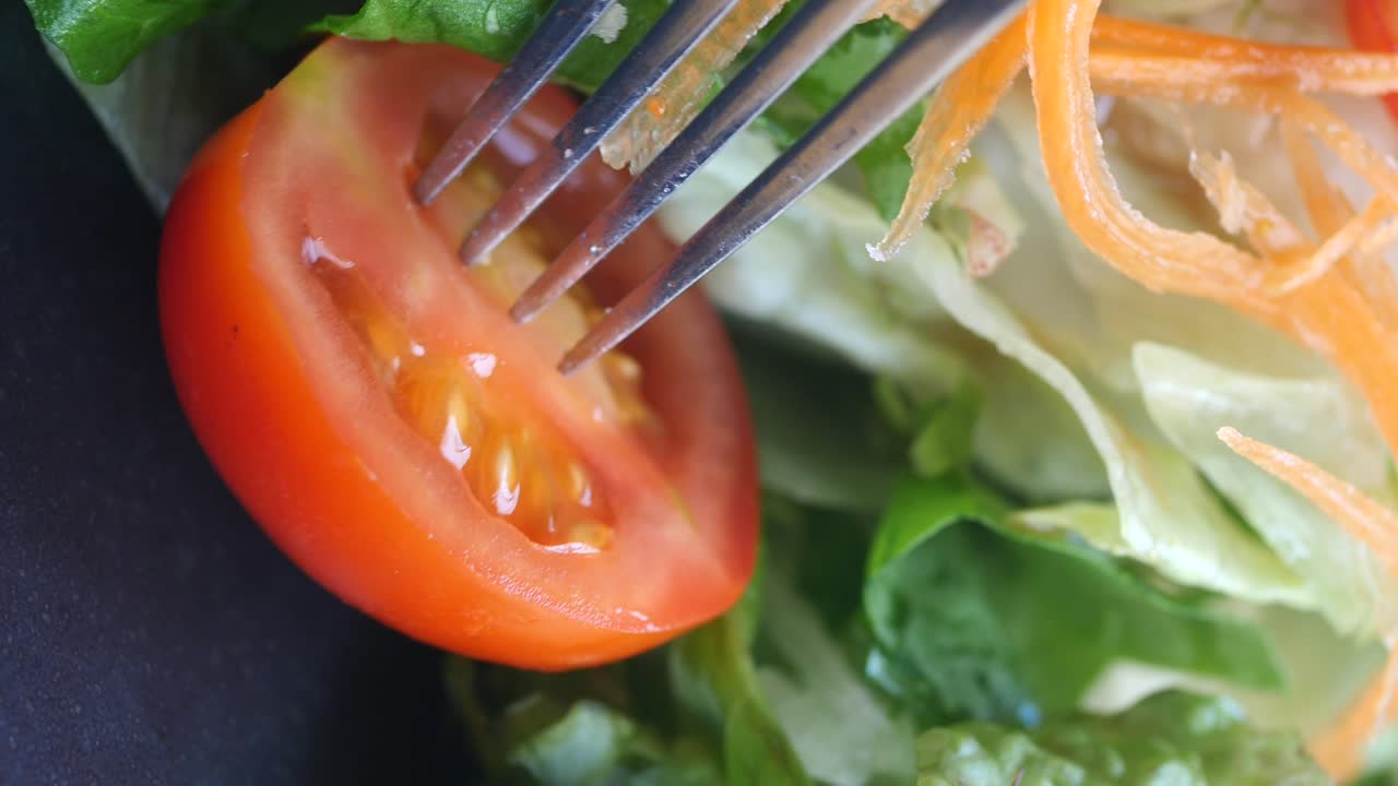 Close-up of a fork picking a tomato slice from a fresh salad