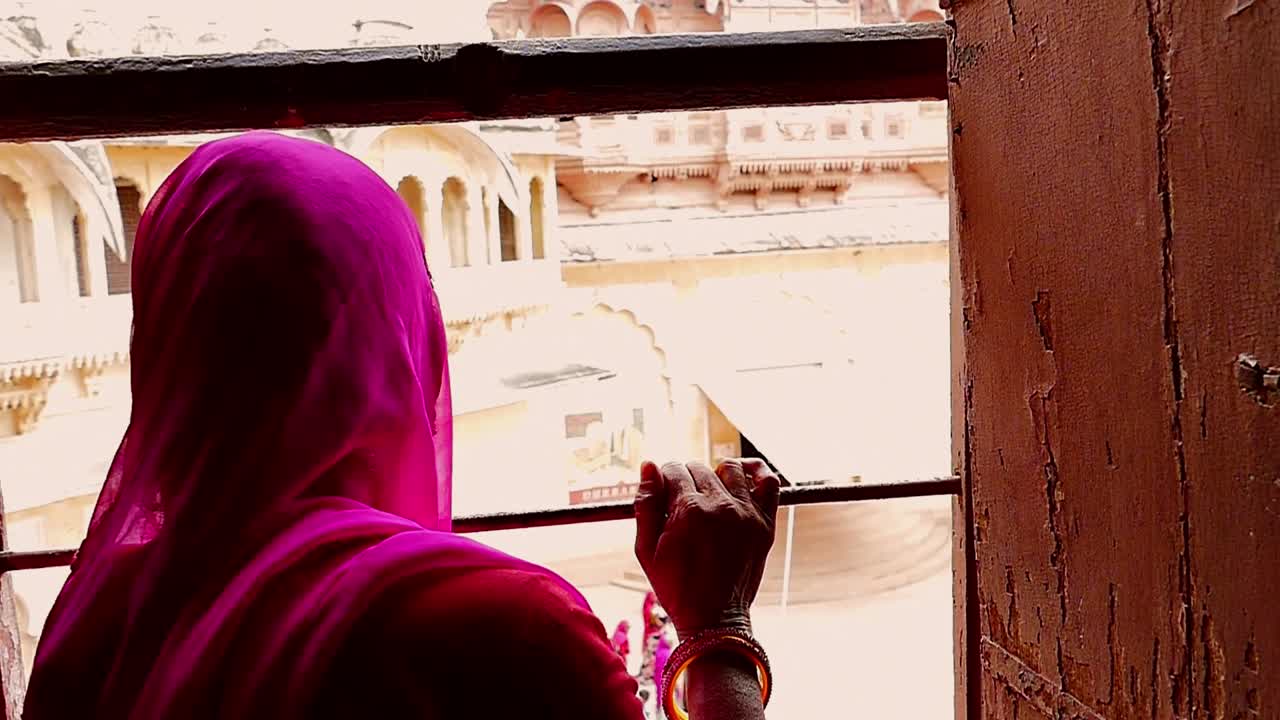 Indian woman curiously watching through the window in the Mehrangarh fort in Jodhpur (India) in slow motion