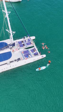 aerial view of a catamaran with people swimming nearby in the turquoise sea of phuket, thailand, under bright daylight