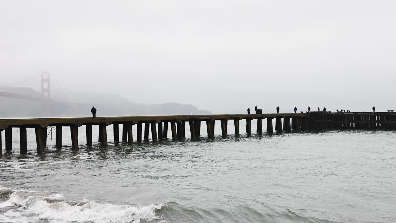 torpedo wharf in the fog with the Golden Gate Bridge and fishermen in the background PAN LEFT