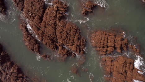 Rising-Aerial-Shot-of-Waves-Crashing-Against-Sandstone-Rocks-from-Birds-Eye-View-Perspective