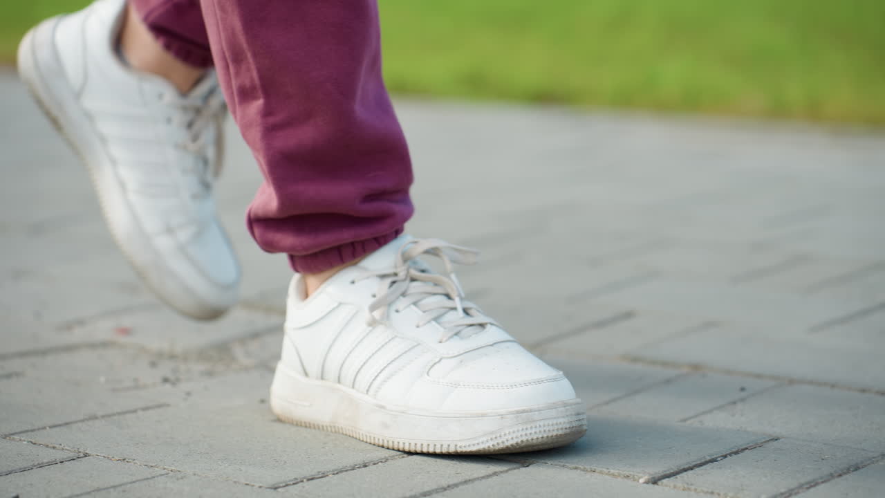 Leg view of fitness coach walking on gray tiled pavement elegantly with gym bag hanging on shoulder under bright daylight capturing athletic stride confidence and casual style in urban autumn setting