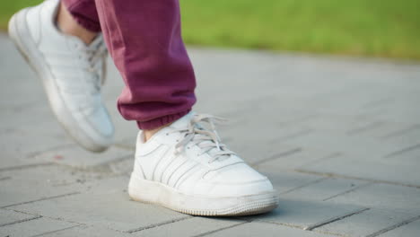 leg view of fitness coach walking on gray tiled pavement elegantly with gym bag hanging on shoulder under bright daylight capturing athletic stride confidence and casual style in urban autumn setting