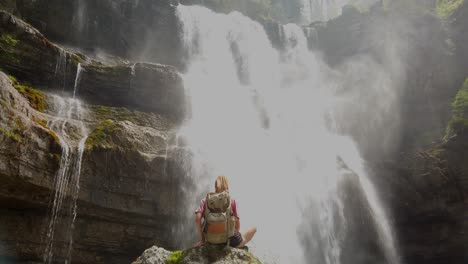 girl hiking is sitting on a rock under a waterfall in a nature reserve