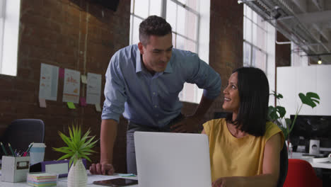 Diverse-male-and-female-business-colleagues-in-discussion-at-work-looking-at-laptop-and-smiling