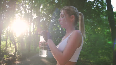 schönes blondes läufermädchen, das eine pause macht, um wasser zu trinken, nachdem es im wald gelaufen ist