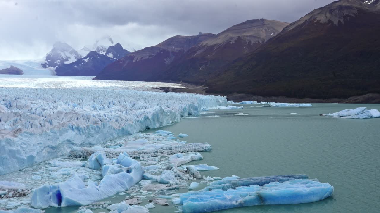 Perito Moreno Glacier with towering ice formations and floating icebergs near Lago Argentino in Los Glaciares National Park. Static view with rugged mountains in the background.
