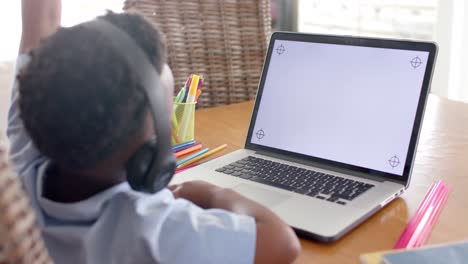 african american boy using laptop, raising hand in online class, slow motion, copy space