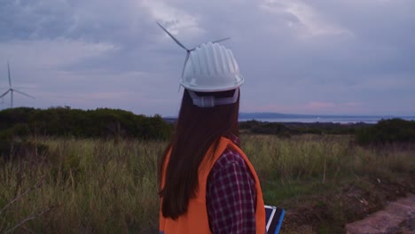 primer plano medio de una ingeniera mirando a su alrededor en una granja de molinos de viento, de mano